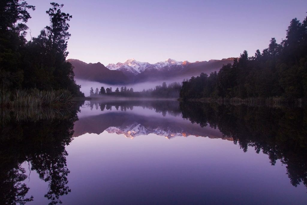 Lago en espejo reflejando montañas nevadas al amanecer